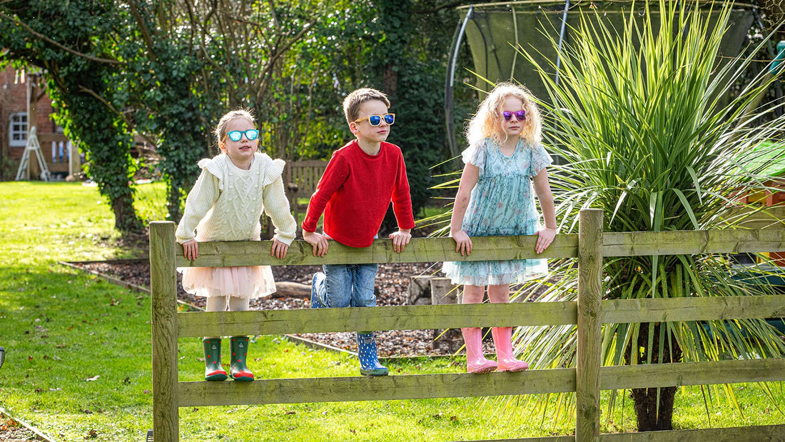 Three Children Stood On Garden Fence In Beautiful Bright Clothing